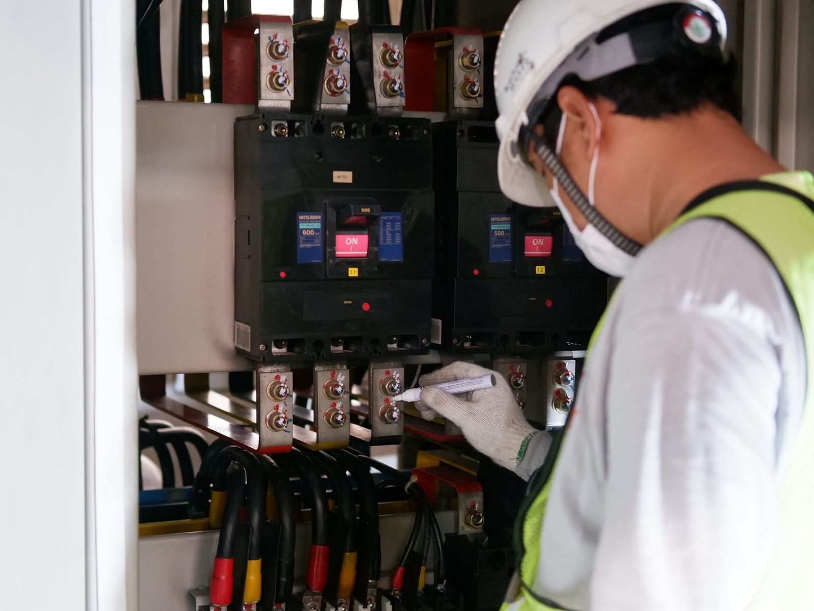 Electrical worker in safety gear inspecting switchgear